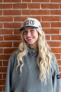 Person wearing a cap with 'KAXI CO' text against a brick wall