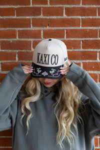 Person wearing a cap with 'KAXI CO' text against a brick wall