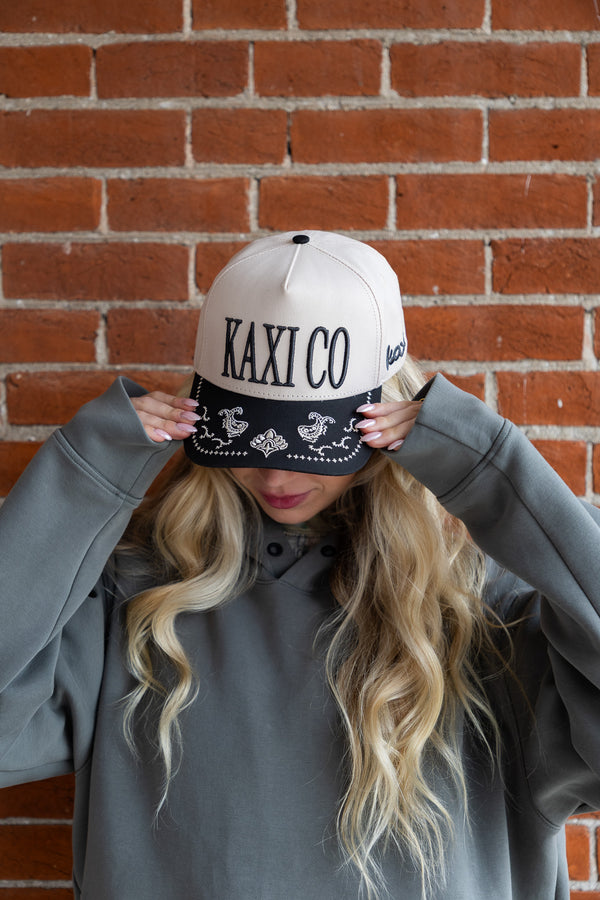 Person wearing a cap with 'KAXI CO' text against a brick wall