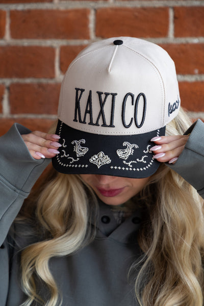 Person wearing a cap with 'KAXI CO' branding against a brick wall.