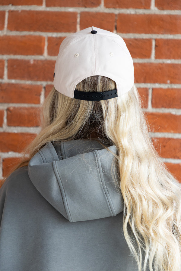 Person wearing a beige cap and gray hoodie with a brick wall background