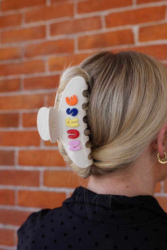 Person with colorful hair clip with "NURSE" writton on it styled on a  french twist against a brick wall.