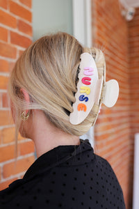Person with a colorful 'NURSE' hair clip in their hair against a brick wall.