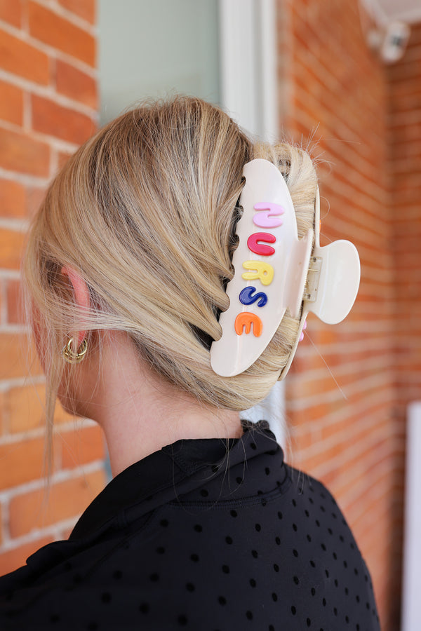 Person with a colorful 'NURSE' hair clip in their hair against a brick wall.