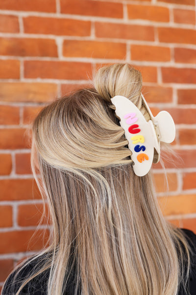 Person with colorful "NURSE" hair clip in hair against a brick wall background