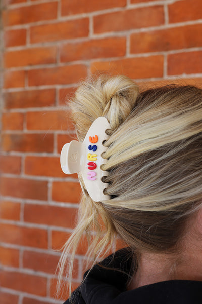 Person with a colorful hair clip spelling "NURSE" in their hair against a brick wall.
