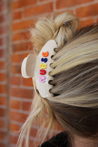 Hair clip with colorful letters in a person's hair against a brick wall background