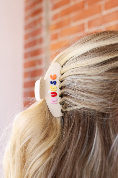Hair clip with colorful letters spelling "NURSE" on a person's hair against a brick wall background