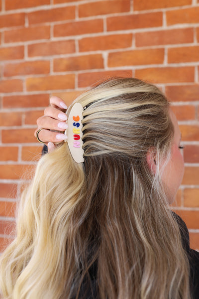 Person with colorful hair clip spelling "NURSE"  in hair against a brick wall