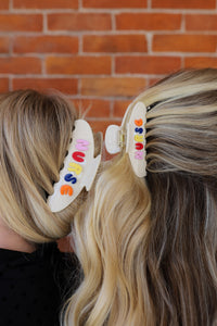 Two people with colorful hair clips in their hair that say "NURSE" against a brick wall.