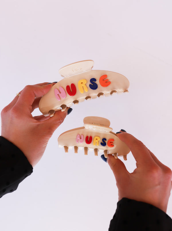 Two hair clips with 'NURSE' letters held by hands against a white background