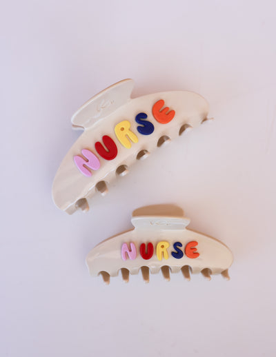 Two cream hair clips with colorful letters spelling 'NURSE' on a light background