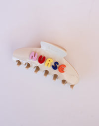 Cream hair clip with colorful letters spelling 'NURSE' on a white background
