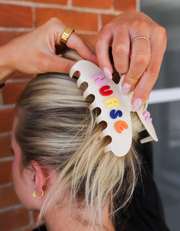 Person putting a cream claw clip in their hair with colorful letters spelling "NURSE" 