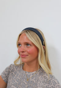 Woman wearing a navy headband with gold studs against a plain background