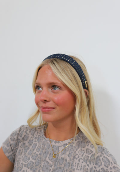 Woman wearing a navy headband with gold studs against a plain background