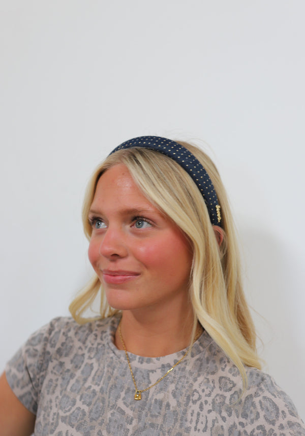Woman wearing a navy headband with gold studs against a plain background