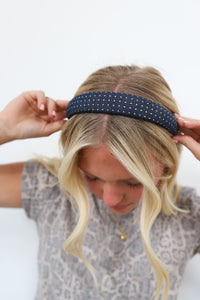 Person wearing a navy headband with gold studs on a white background