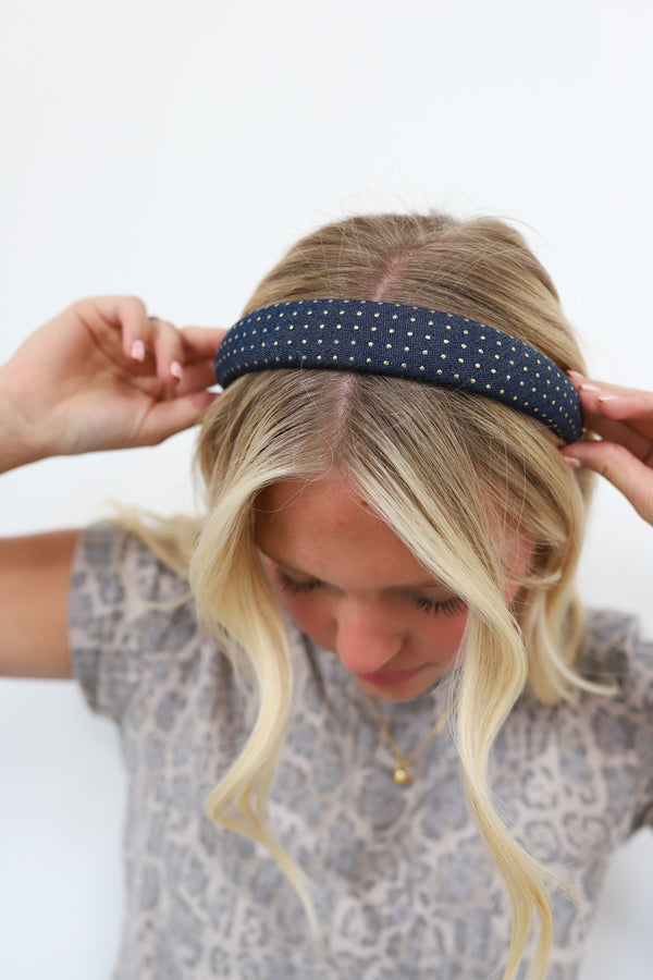 Person wearing a navy headband with gold studs on a white background