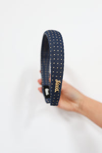 Navy blue headband with gold studs held by a hand on a white background