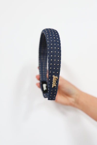 Navy blue headband with gold studs held by a hand on a white background