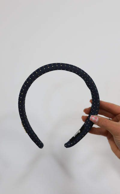 Denim headband with gold studs held against a white background.