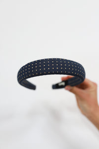Denim headband with gold studs held by a hand on a light gray background