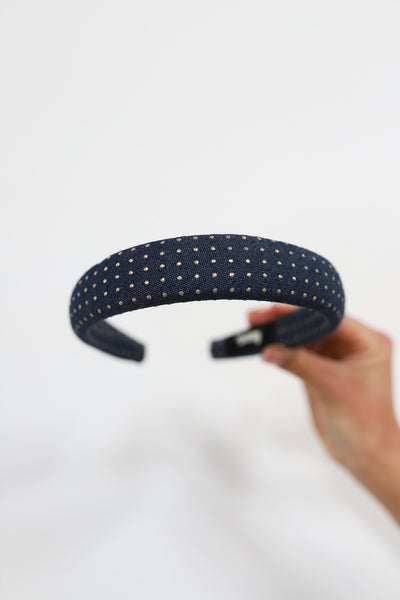 Denim headband with gold studs held by a hand on a light gray background
