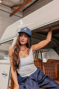Woman sitting inside a vehicle wearing a white tank top and denim blue star baseball cap with a teddy bear embroidered on the front