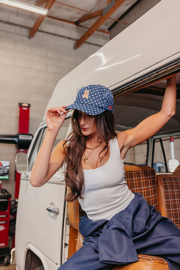 Woman wearing a blue denim star baseball cap sitting in front of a white van in a garage.