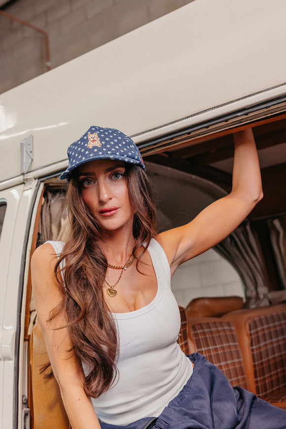 Woman wearing a denim star baseball cap with a teddy bear embroidered on it  and sitting inside a vehicle.