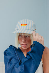 Person wearing a blue and white striped cap with a hot dog design against a light blue background