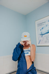 Person wearing a cap and blue jacket in a bathroom with a poster on the wall.