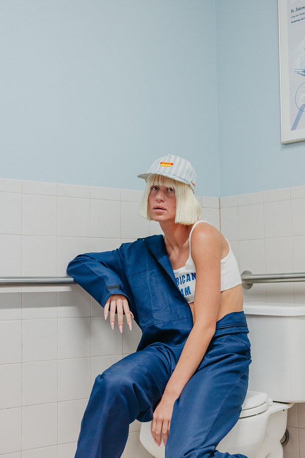 girl wearing blue and white striped baseball cap with a hot dog embroidered on the front