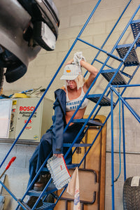 Person on a ladder in a garage with automotive products in the background