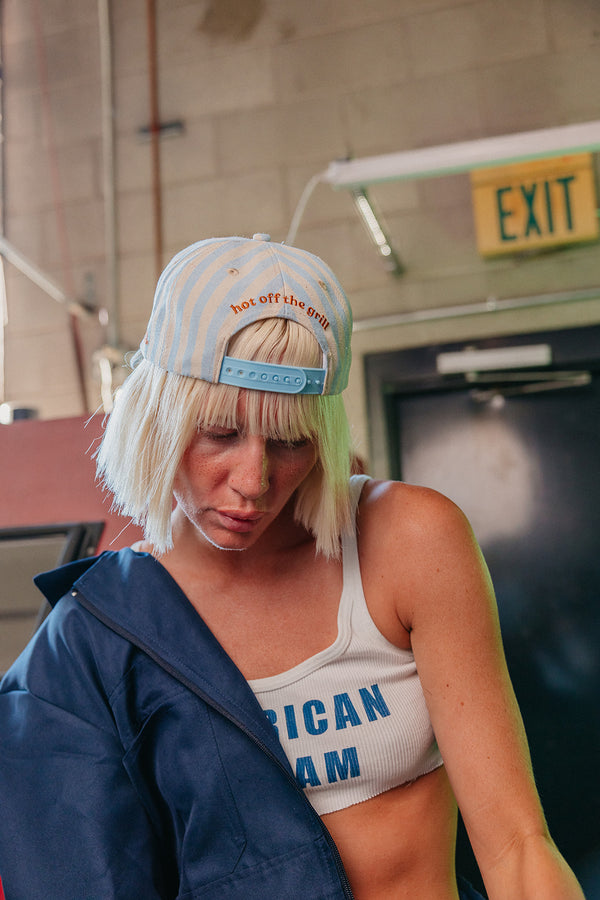 blue and white striped baseball cap being worn backwards, "hot off the grill" embroidered on the back