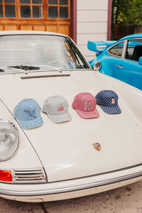 Four colorful baseball caps on a classic white car with a blue car in the background.