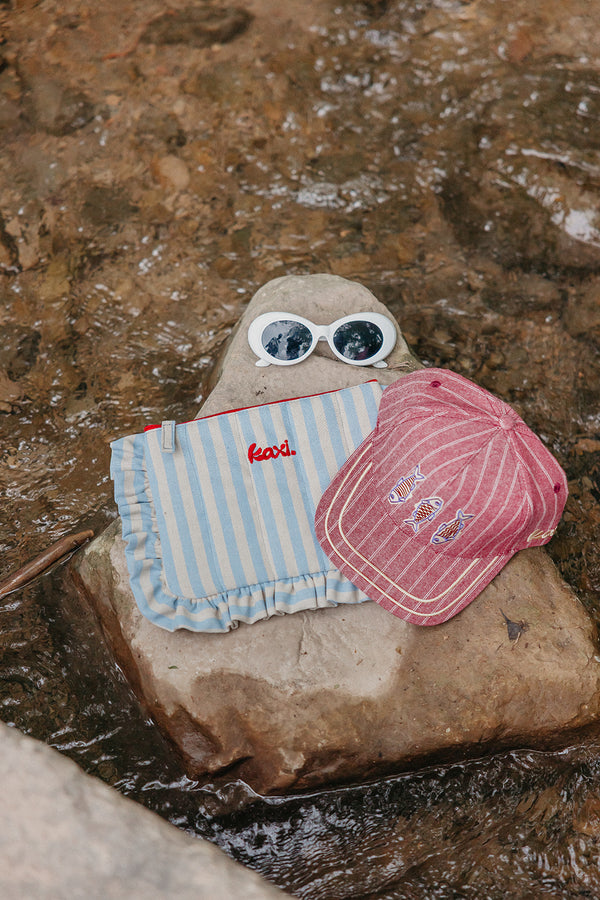 Rock with red trucker hat, white sunglasses, and striped cosmetic bag on it
