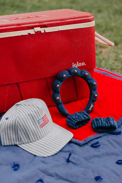 striped baseball cap with an American flag embroidered on it next to a navy blue studded "get ready with me" headband and matching wristies