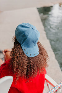 Person wearing a blue cap with star studs, standing by a waterfront.