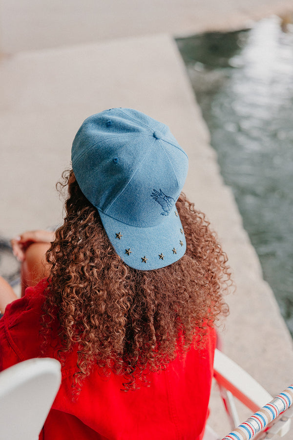 Person wearing a blue cap with star studs, standing by a waterfront.