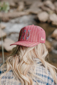 Person wearing a red cap with fish designs outdoors
