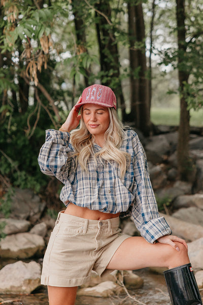 Woman in plaid shirt and shorts with a red trcuker hat with fish embroidery outdoors