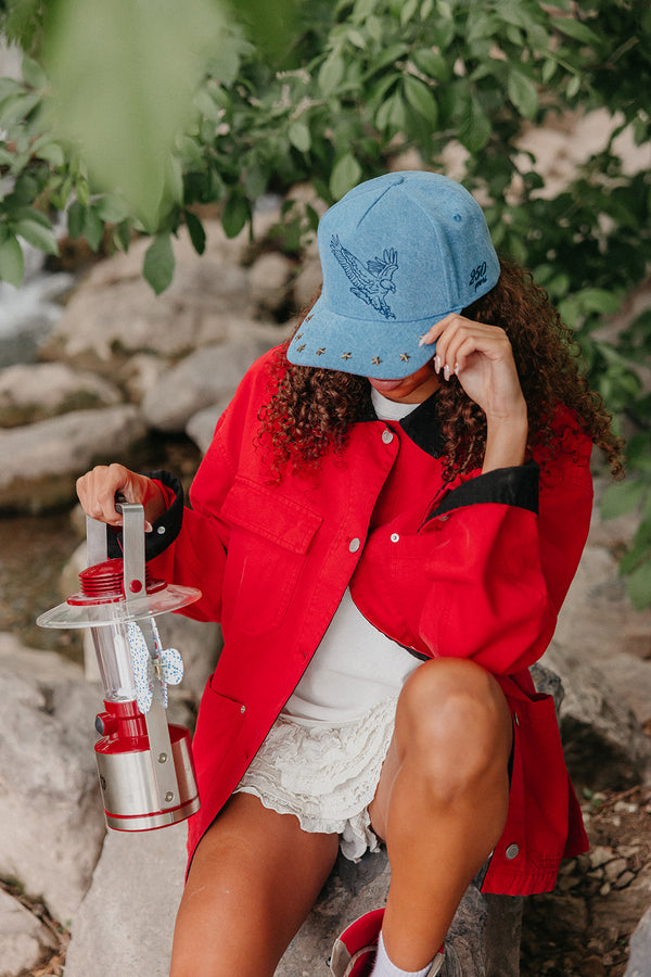 Person wearing a red coat and denim blue trucker hat with an eagle on it holding a lantern outdoors