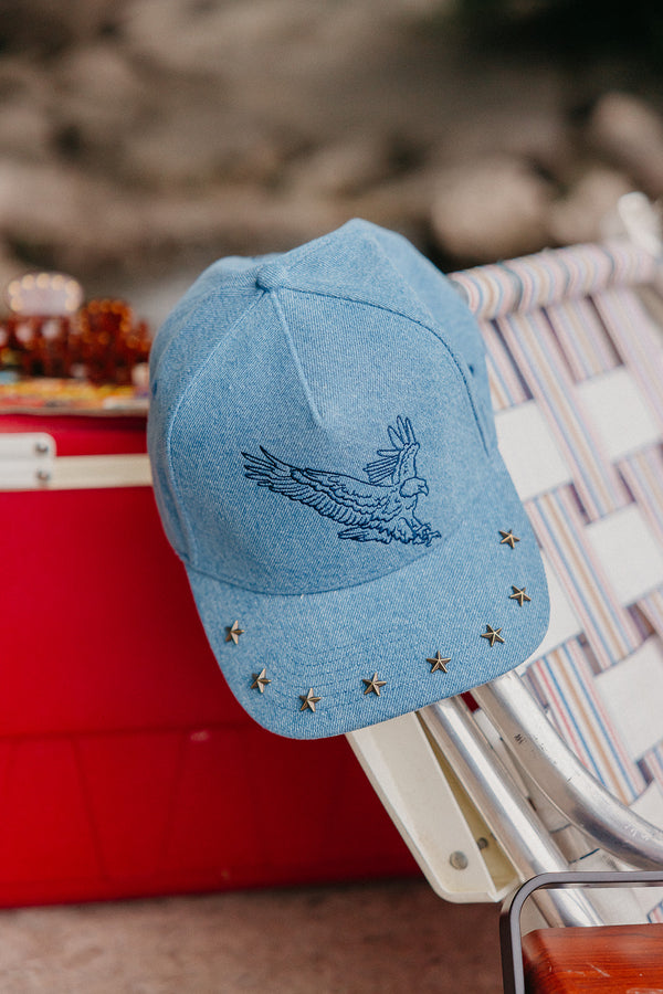 denim trucker hat with an eagle embroidered on it, with studs on the brim