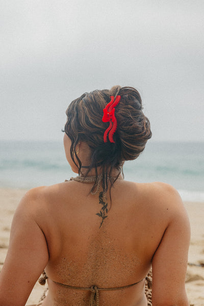 Person with French twist hair and a red hair accessory standing on a beach.