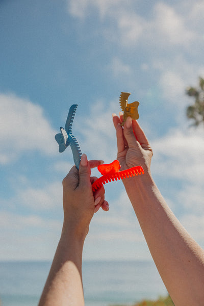 Two hands holding colorful wavy hold everything claws against a blue sky with clouds.