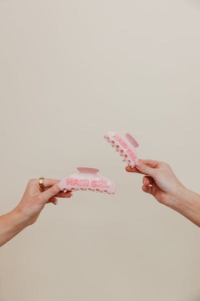 Two hands holding a pink hair clip against a beige background