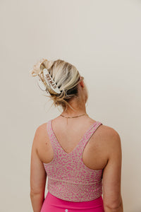 Person wearing a pink leopard print sports bra and pink shorts against a beige background wearing brown and cream Gym Girl claw