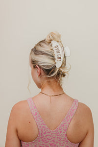 Person wearing a pink leopard print tank top with a white claw clip that says 'GYM GIRL' on a plain background.